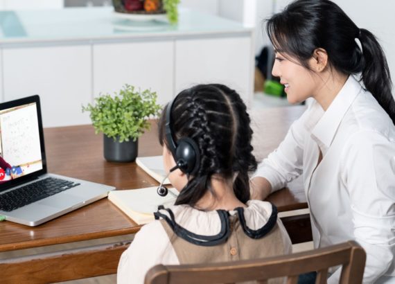 Mother helps her elementary-school age daughter with her online learning classes.