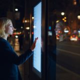 A woman uses an interactive panel in a smart city at night.