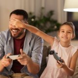 A father and daughter play a video game in their living room.