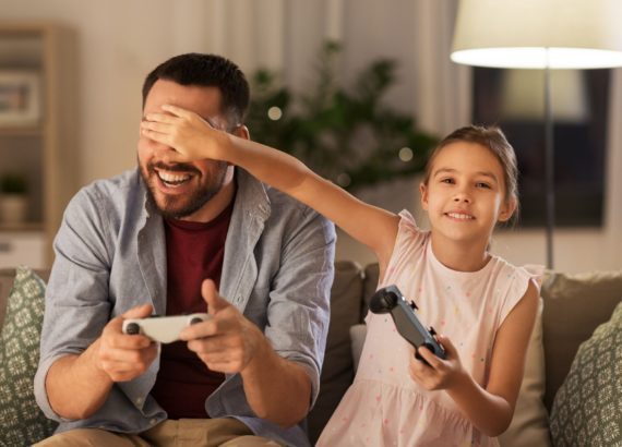A father and daughter play a video game in their living room.
