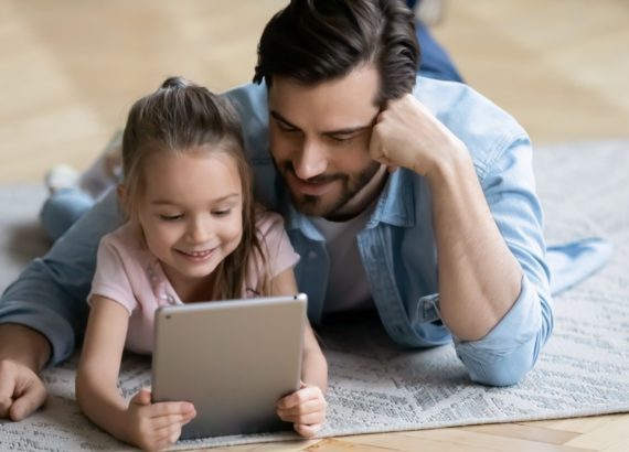 A father and daughter watch a kid's show on a tablet together.