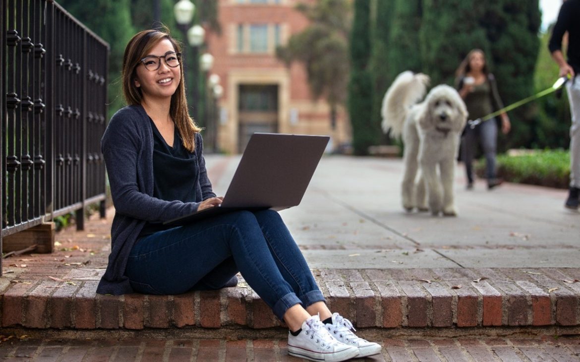 Woman sitting on the ground, using a laptop with a dog in the background