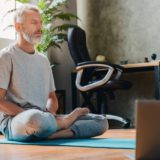Man meditating on a yoga mat in front of a laptop