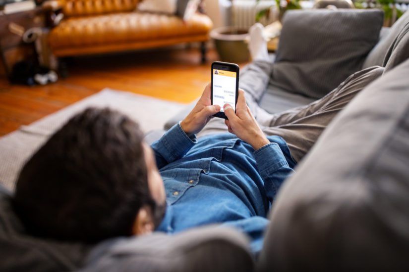 A man practicing online dating safety tips while lying on the couch.