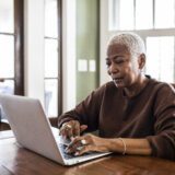 An older woman browses her laptop using symmetrical speeds.