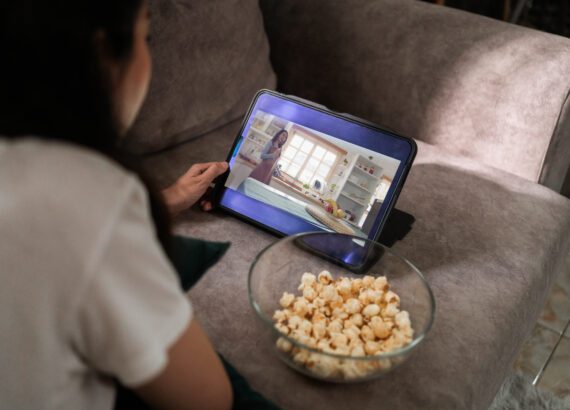 Women streaming tv on tablet while on couch eating popcorn.