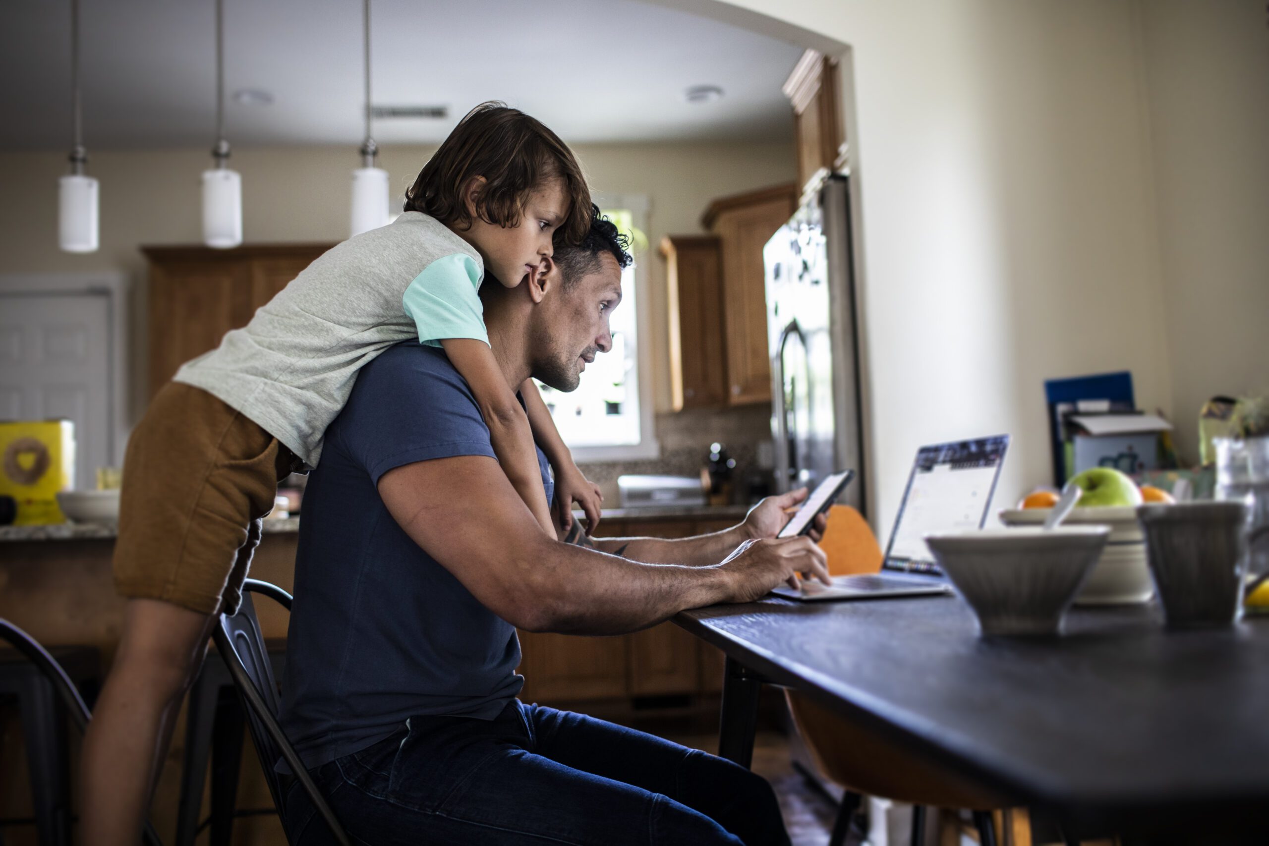 Father using laptop while son looks over his shoulder Dad and child in home office