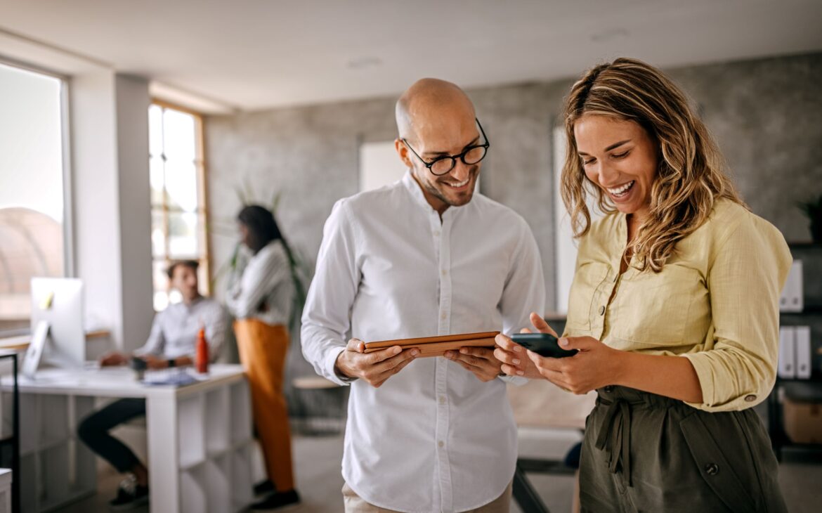 Man and woman standing in office space looking at devices
