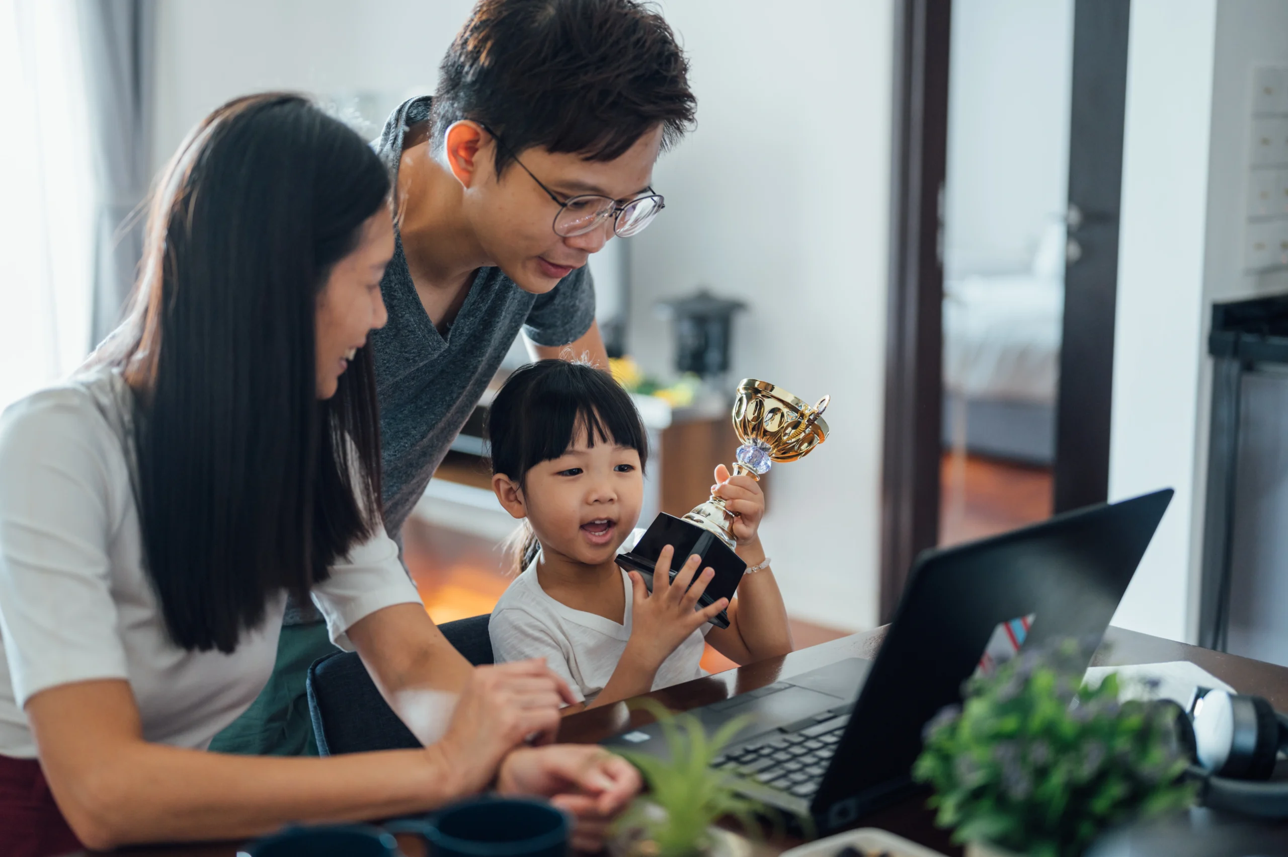Family playing together on computer with child holding a trophy