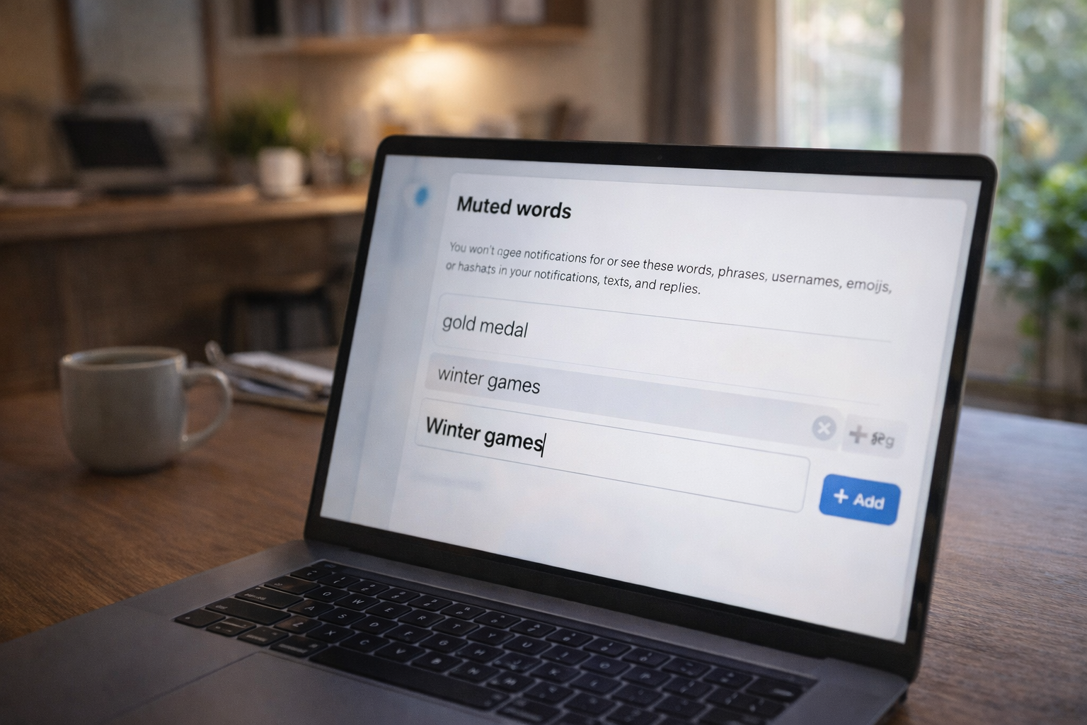 A laptop on a wooden desk showing a social media settings page for muted words. The terms "gold medal" and "winter games" are being added to the list to help avoid spoilers