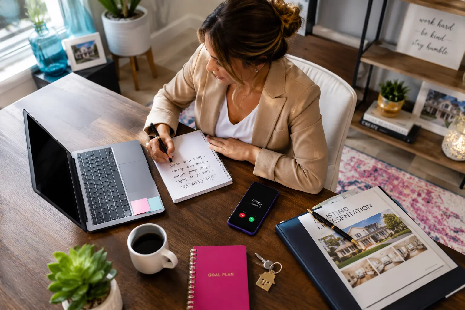 A real estate professional working at a modern home office desk with a laptop, notebook, coffee, and smartphone showing an incoming call.