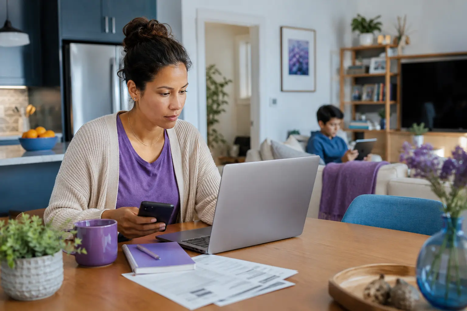 A woman reviewing household expenses on a laptop and smartphone while a child uses a tablet in the background.